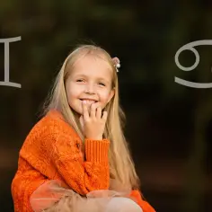 Uśmiechnięta dziewczynka w pomarańczowym swetrze, z symbolami Bliźniąt i Raka. Czyżby urodzona 21 czerwca?