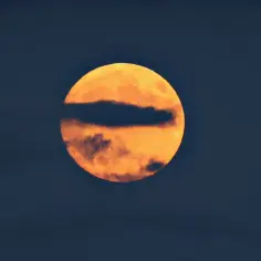Pomarańczowa pełnia księżyca, częściowo zasłonięta przez ciemną chmurę. Wygląda jakby zbliżał się najbliższy nów księżyca.
