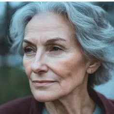 Portret starszej kobiety z siwymi włosami, spoglądającej w bok. Jej twarz jest pełna zmarszczek, co sugeruje mądrość i doświadczenie. Może to być ilustracja do horoskop wodnik 2026.